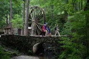 People walking past windmill and river in forest