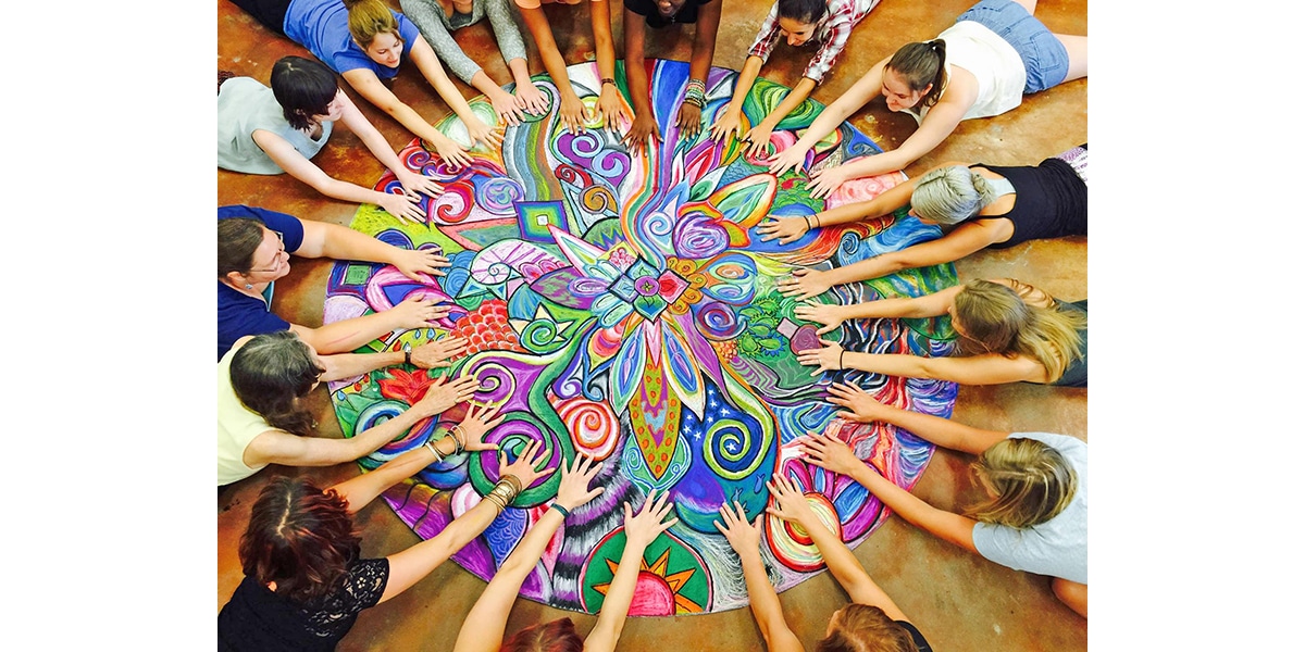 Students in a circle reaching towards center of art drawn on the ground