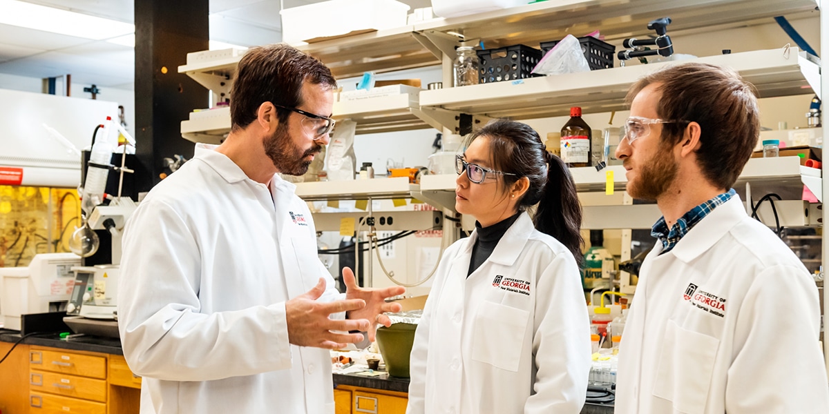 College students in lab coats speaking to male professor