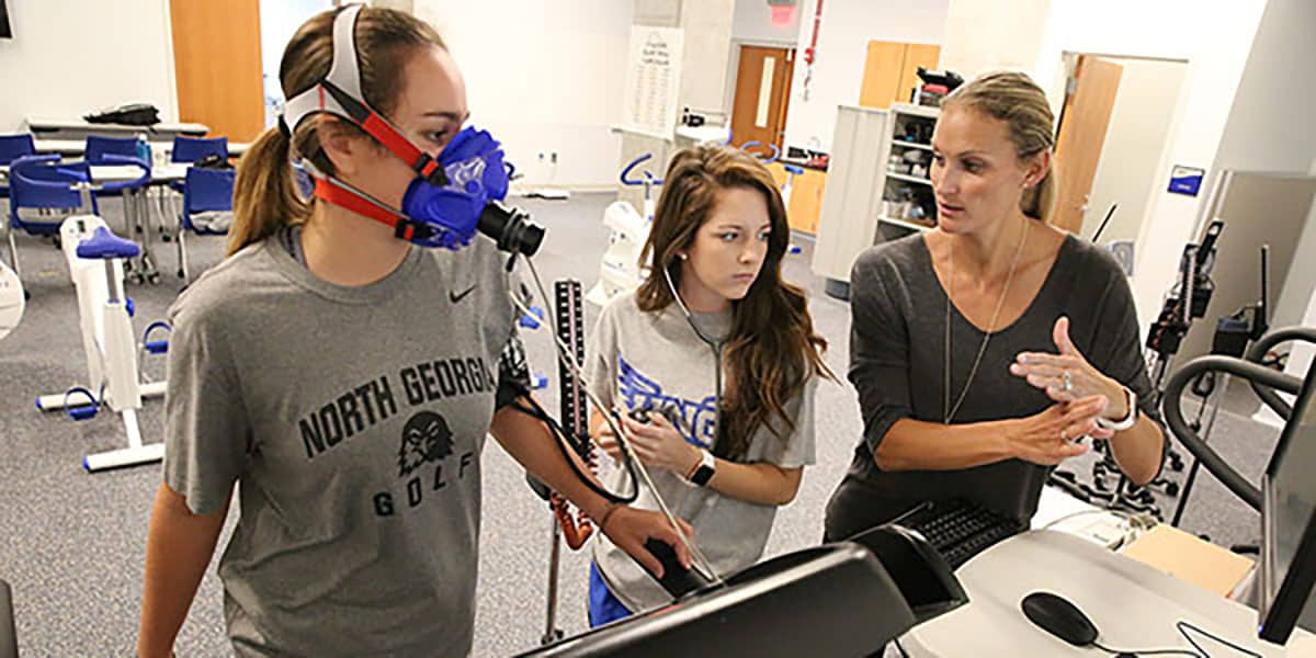 Students and female professor working with exercise equipment in classroom