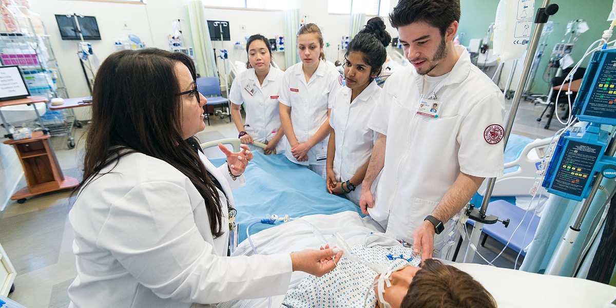 Nursing students working with dummy patient in mock hospital room