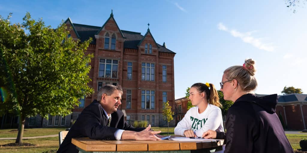 College students and professor sitting at table outdoors on campus