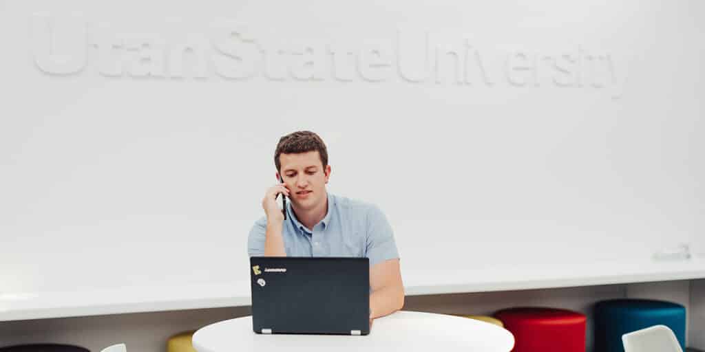 College student talking on the phone and working on laptop in college room