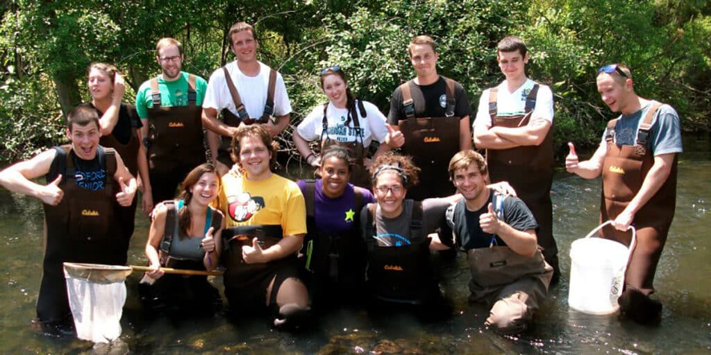 Group of students standing in river and smiling